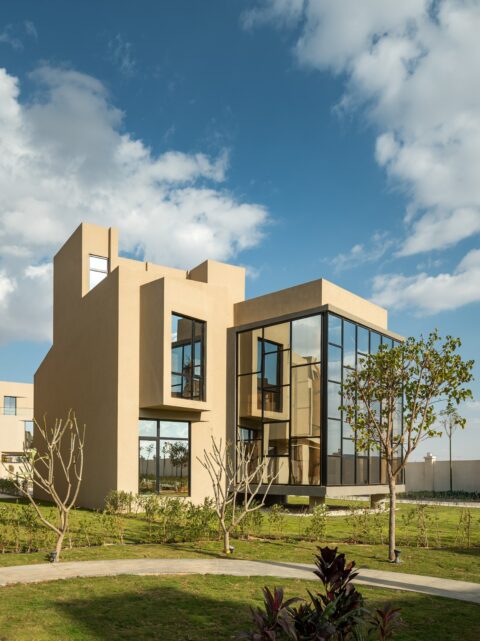 Modern residential villas with contemporary architecture, large glass facades, and landscaped green spaces under a clear blue sky